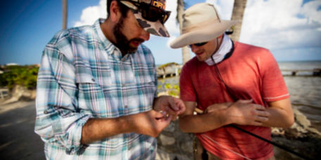 An instructor shows an angler a fly, palm trees in the background