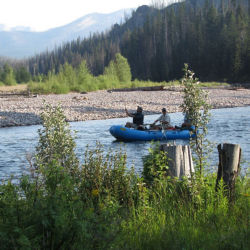 Two anglers fly fish from a blue raft on a river in Montana.