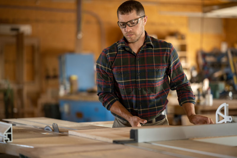Man wearing a red flannel shirt working in a wood shop.