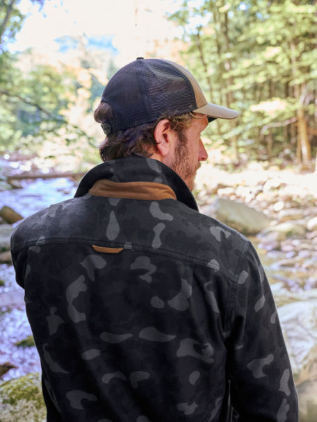 Man overlooks a forested stream in an Orvis Blackout Camo Flannel