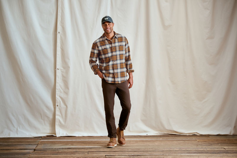 A man with his hand in a pocket wearing a brown plaid shirt and brown pants.