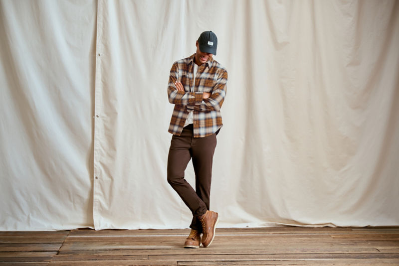 A model wearing a flannel shirt with chocolate brown 5-Pocket pants and work boots.
