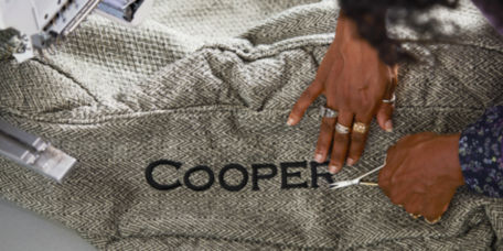 A closeup of hands at work, trimming embroidery threads around the name Cooper embroidered on a dog bed.