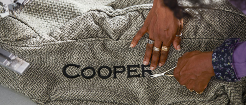 A closeup of hands at work, trimming embroidery threads around the name Cooper embroidered on a dog bed.