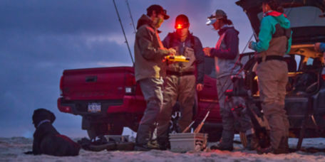 A group of early-morning anglers prep their gear behind their pick-up truck.