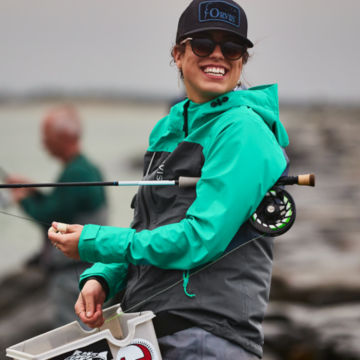 Angler wearing Women's Ultralight Wading Jacket adjusts her line along a rocky wharf.