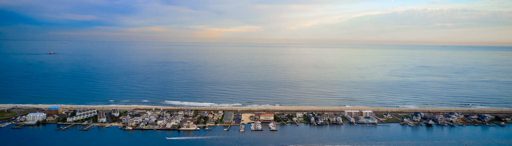 An aerial shot of a breakwater on the ocean with houses.