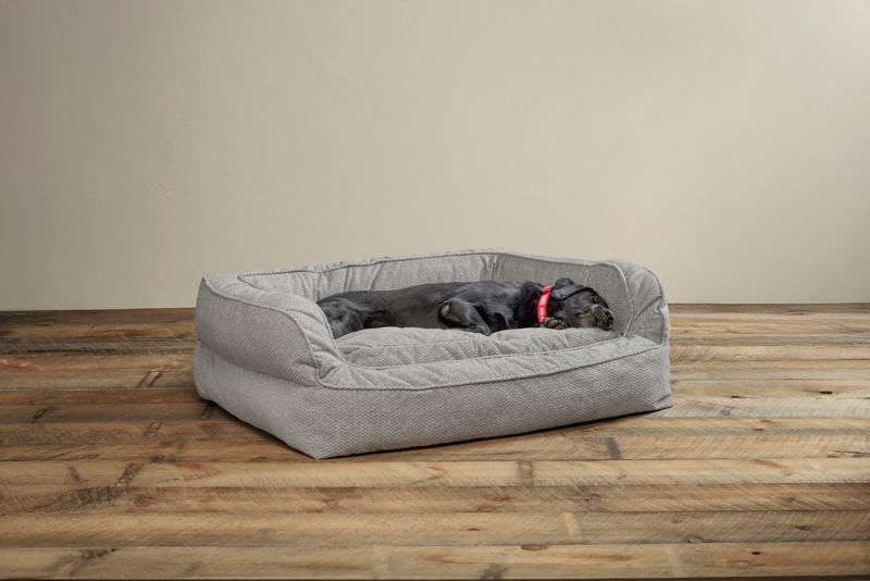 An elderly labrador sleeps soundly in a gray couch bed.
