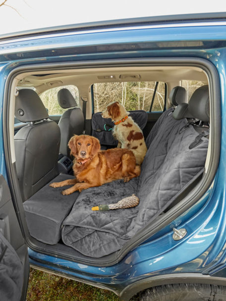 Two muddy dogs sit on top of Quilted Backseat Protector in back of SUV.