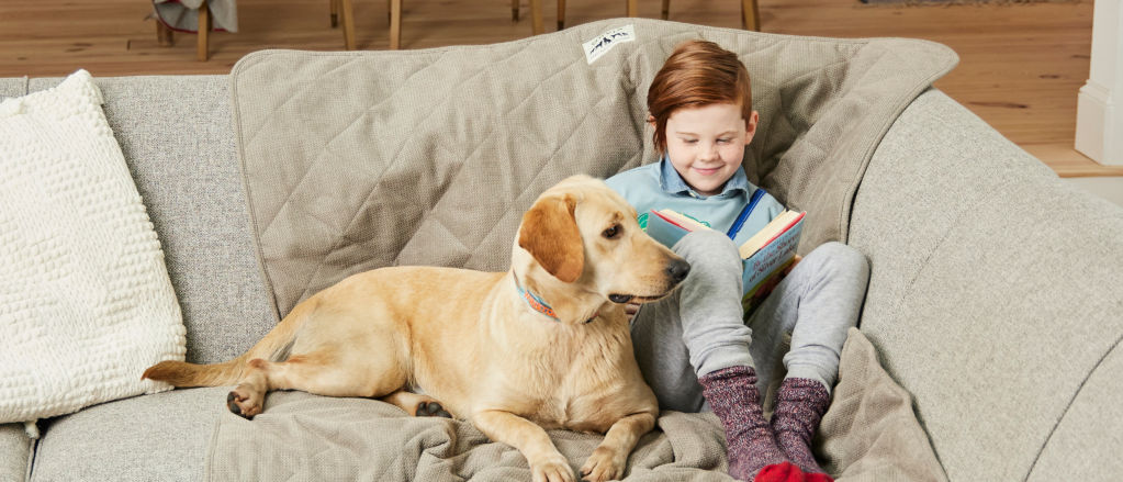 A young child sitting on the couch next to her yellow lab