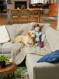 A young girl sitting on the couch with a furniture protector next to her yellow lab