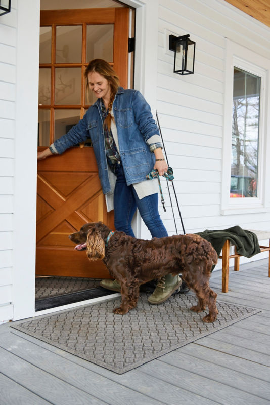 A curly-haired water spaniel stands on a Water Trapper mat as they're let into the house.