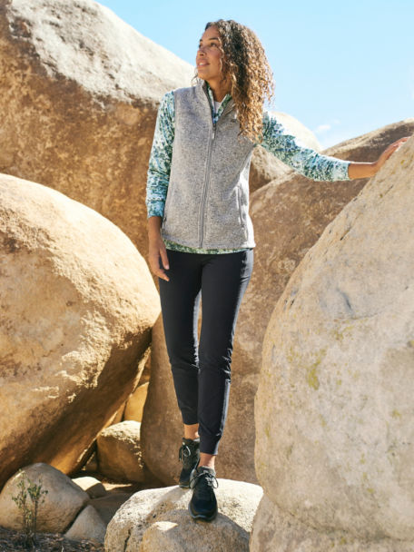 Woman in Grey R65 Sweater Fleece vest hops down some rocks in the desert.
