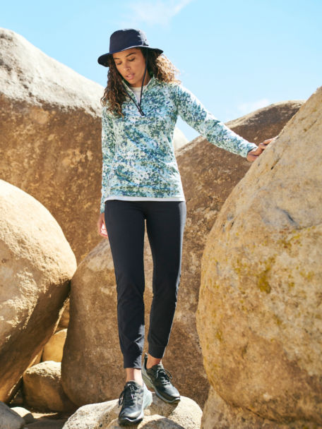 Woman in Grey R65 Sweater Fleece vest hops down some rocks in the desert.