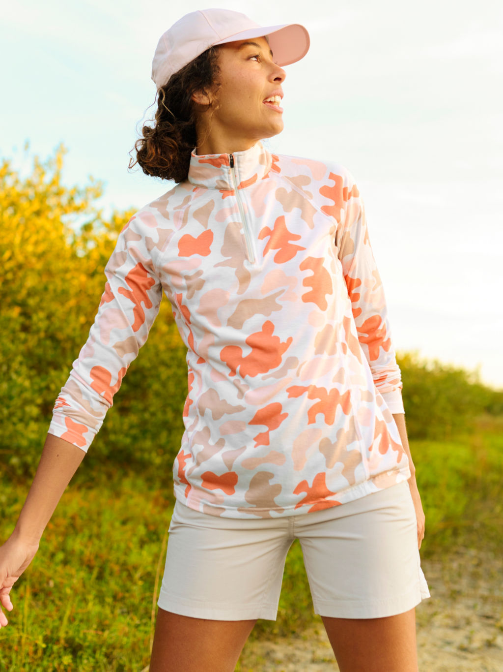 A hiker wearing a colorful camo drirelease shirt looks back over her shoulder on a bright day.