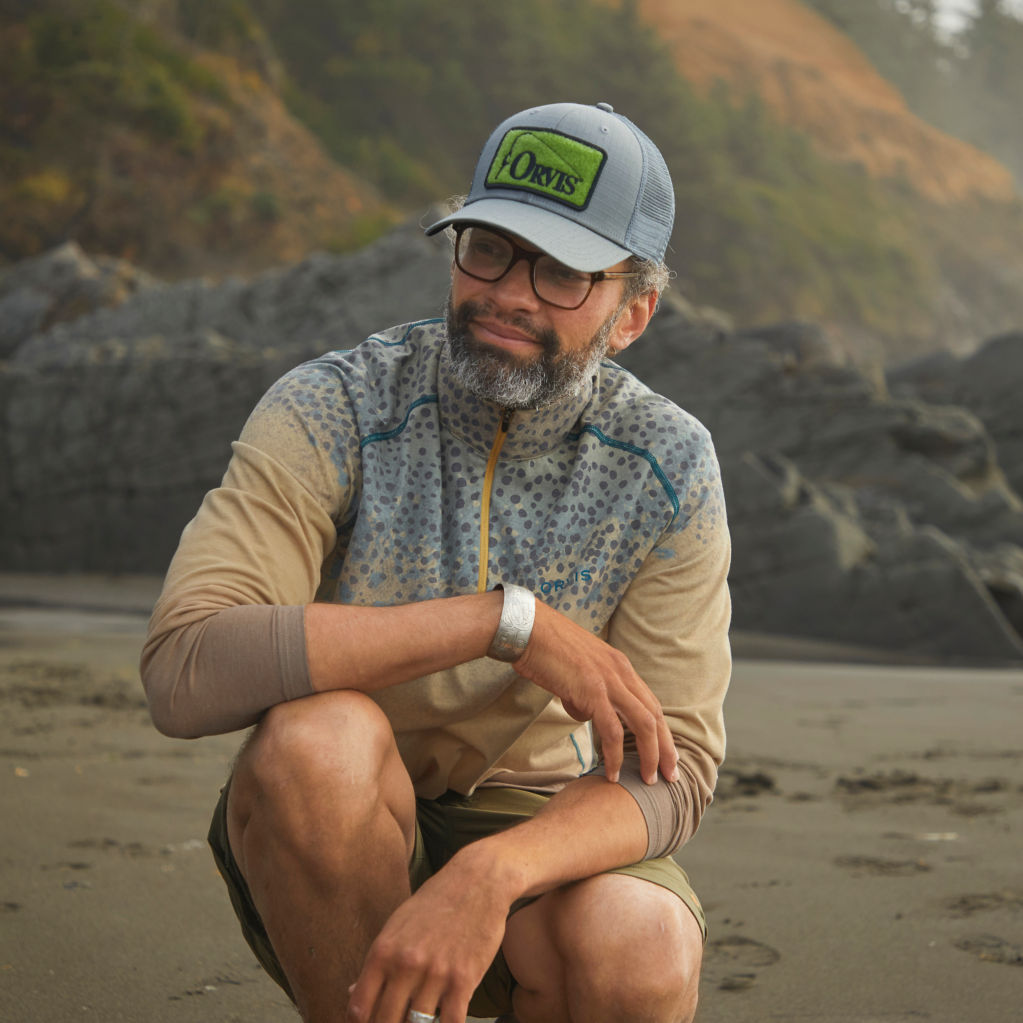Man in Trout Print drirelease® Printed Quarter-Zip takes a moment to reflect on the beach.
