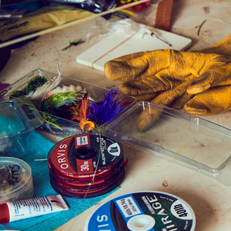 A table of fly tying materials including a fly box and leather glove.