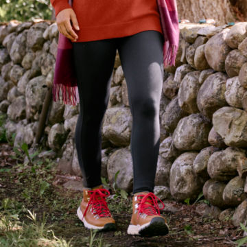 Woman in On Repeat Leggings walks through the woods along the a rock wall.