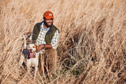 A man kneeling in a field holds a dog's collar