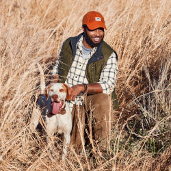A man kneeling in a field holds a dog's collar