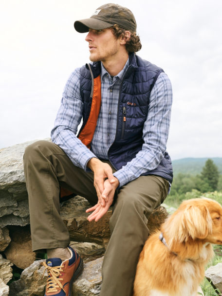 Man in Navy Recycled Drift Vest sits on a rock and surveys the landscape with his dog.