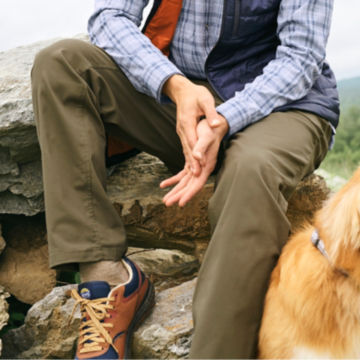 Man in Tarragon O.O.O.O Pants sits on a rock with his dog.