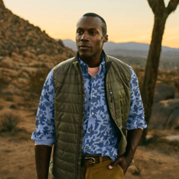 Man in blue camo-patterned tech chambray shirt wanders down a desert trail in the early morning.
