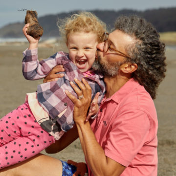 A man holds up his daughter on the beach.