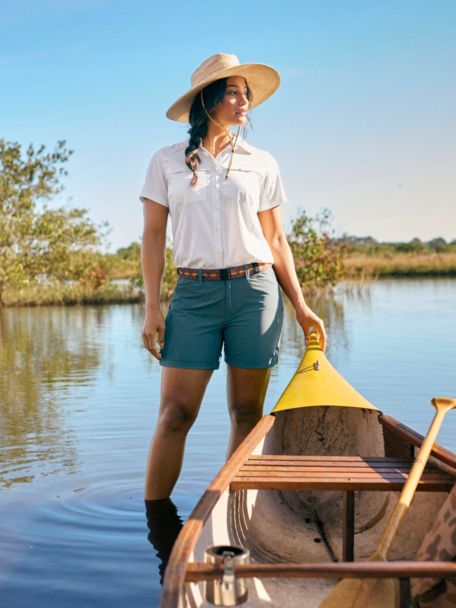 Woman in White Open-Air Caster Short-Sleeved Shirt wades in marsh next to rowboat.