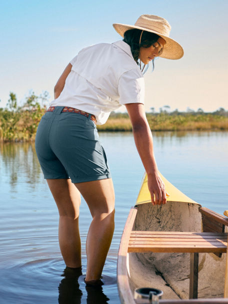 Woman in White Open-Air Caster Short-Sleeved Shirt wades in marsh next to rowboat.