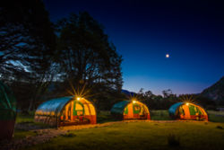 Tents at base camp in the dark glowing from within under a moon