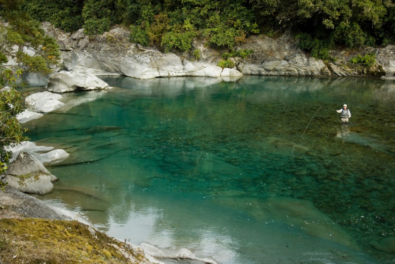 A man fishing in a gorgeous green inlet surrounded by rocky slopes.