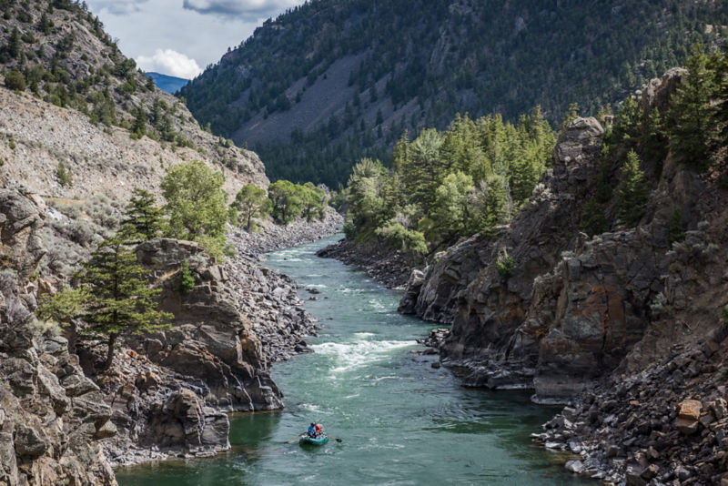 A group of anglers paddle down a river between steep rocky mountains.