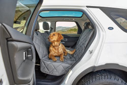 A dog sitting on a seat protector in the back of a car