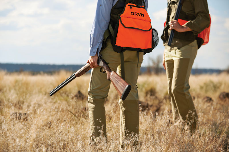 Hunters survey a field in a photo from the waist down.