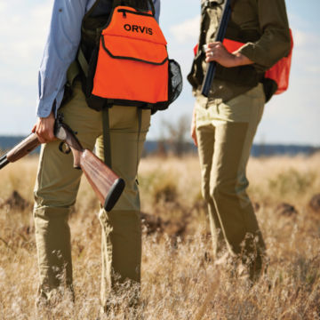 Hunters survey a field in a photo from the waist down.