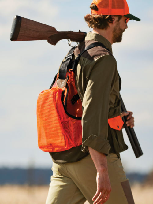 A hunter wearing a Waxed Cotton Strap Vest walks through high brush.