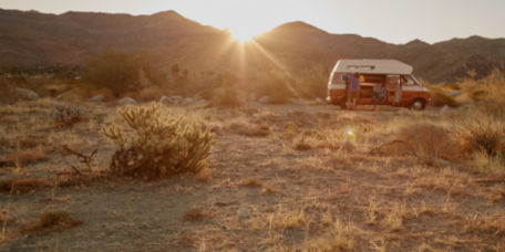 A camper van parked in the desert with the setting sun behind