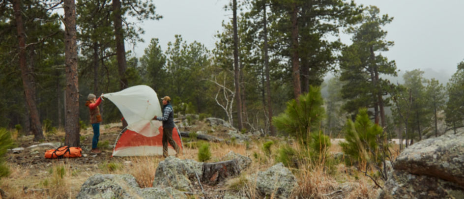 Two people pitching a tent in the woods.