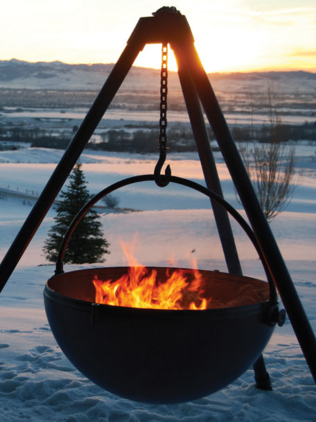 Lit Cowboy Cauldron sits on top of a snowy field against the backdrop of a falling Sun.