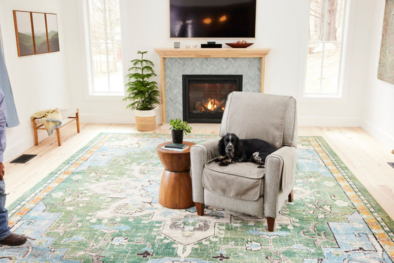 A black dog sitting on a furniture protector covering a chair in a living room 