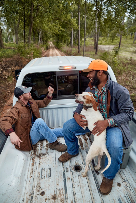 Two men talking in the back of a truck with a dog.