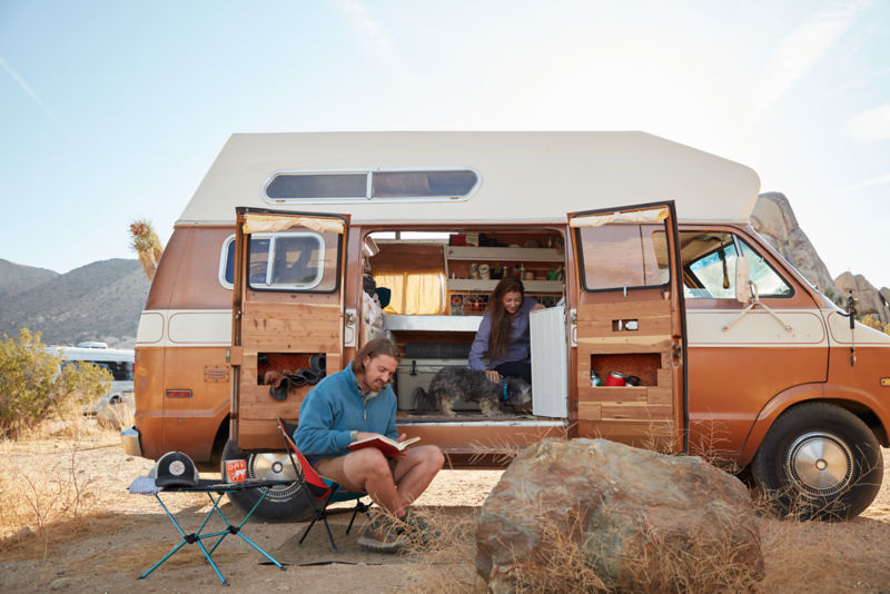 Man reading a book outside of a van in the desert.
