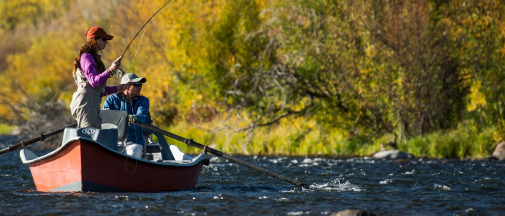 Two anglers fly fishing from a row boat on the water.