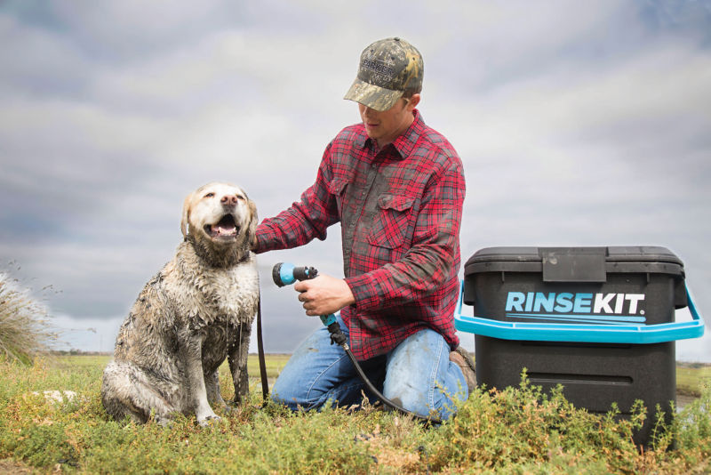 A man kneeling in the grass showering off his muddy dog