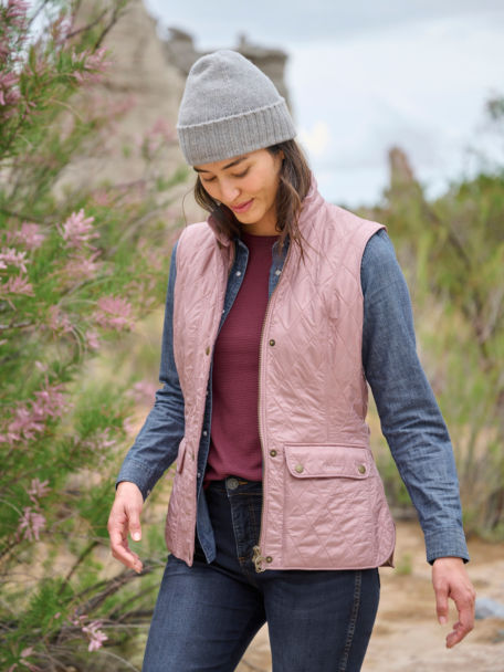 Woman in Barbour Wray Gilet walks throguh a pine tree path.