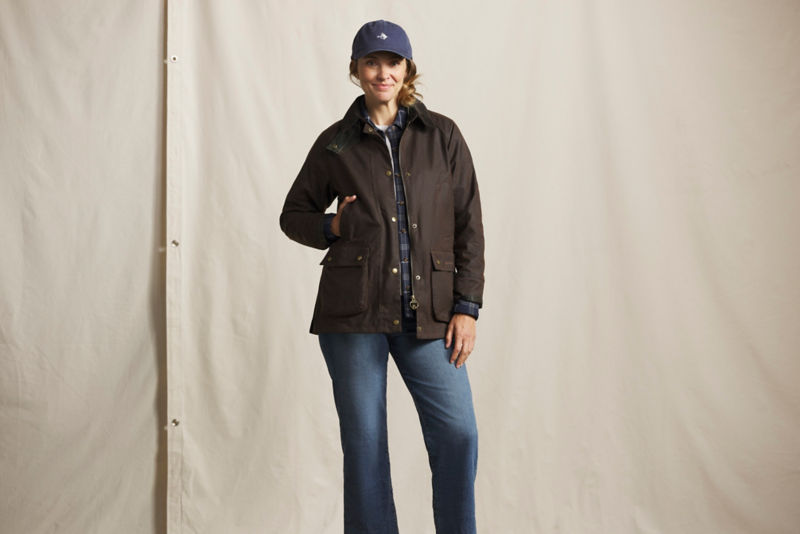A model wearing a brown Barbour jacket over a blue plaid shirt and blue jeans.
