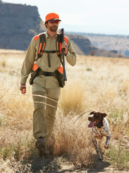 Man and his dog walk out of a high grass field after being out on the hunt.