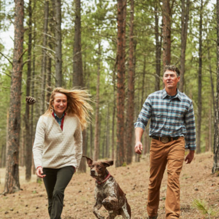 Couple tosses a pinecone for a dog in the woods