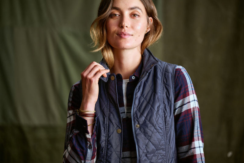 A model wearing a blue and burgundy plaid flannel shirt topped by a blue quilted vest.